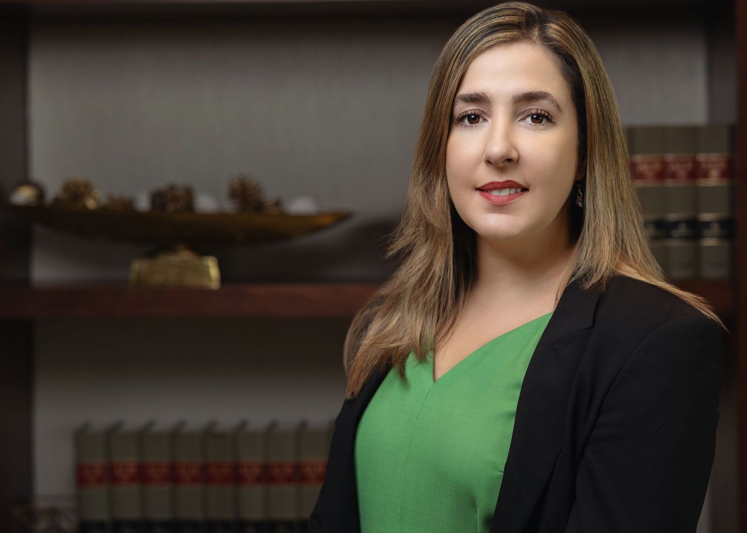 Professional woman in green blouse and black blazer in law office setting.
