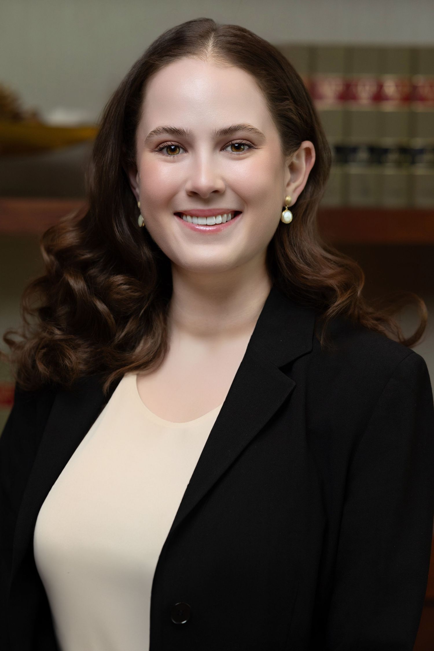 Smiling young female attorney in black blazer before law library bookshelf.