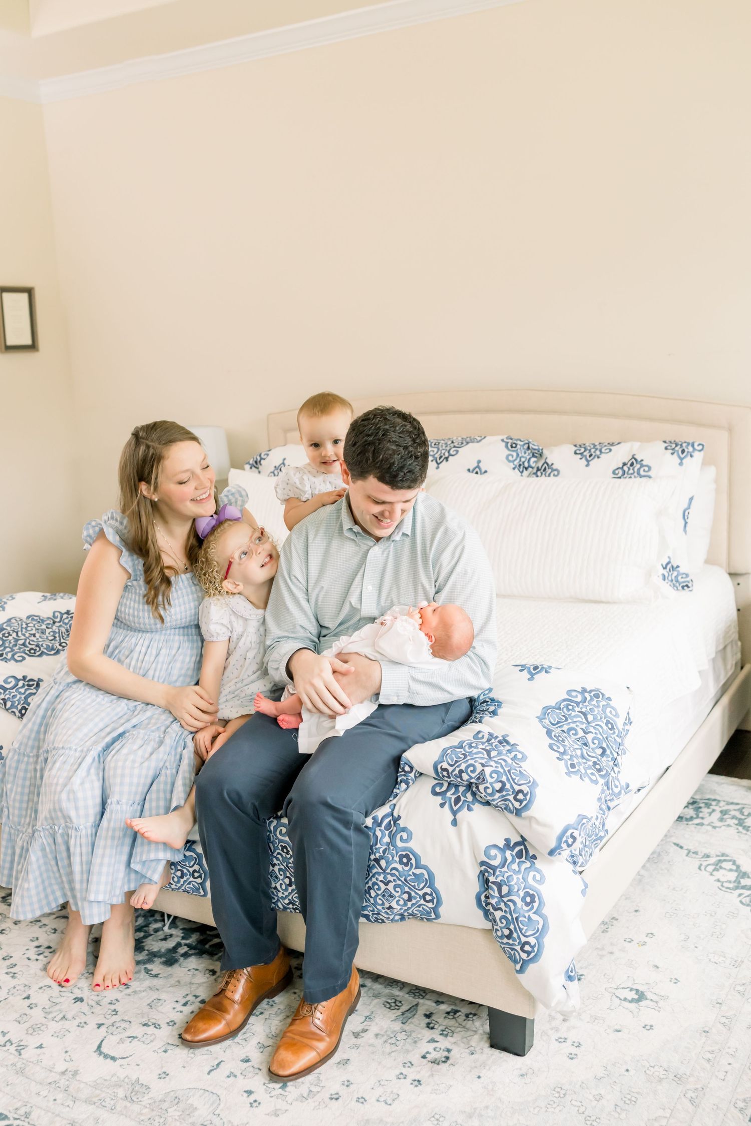 A family sits together on a blue and white patterned bed in a bright, airy room.
