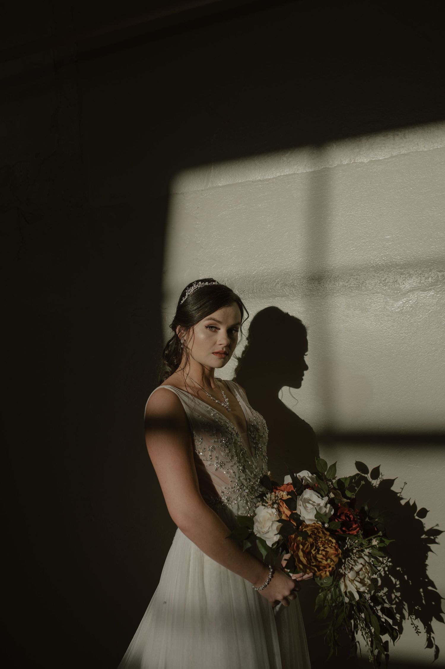 A bridal portrait with dramatic shadow play featuring a luxurious bouquet against a white wall.