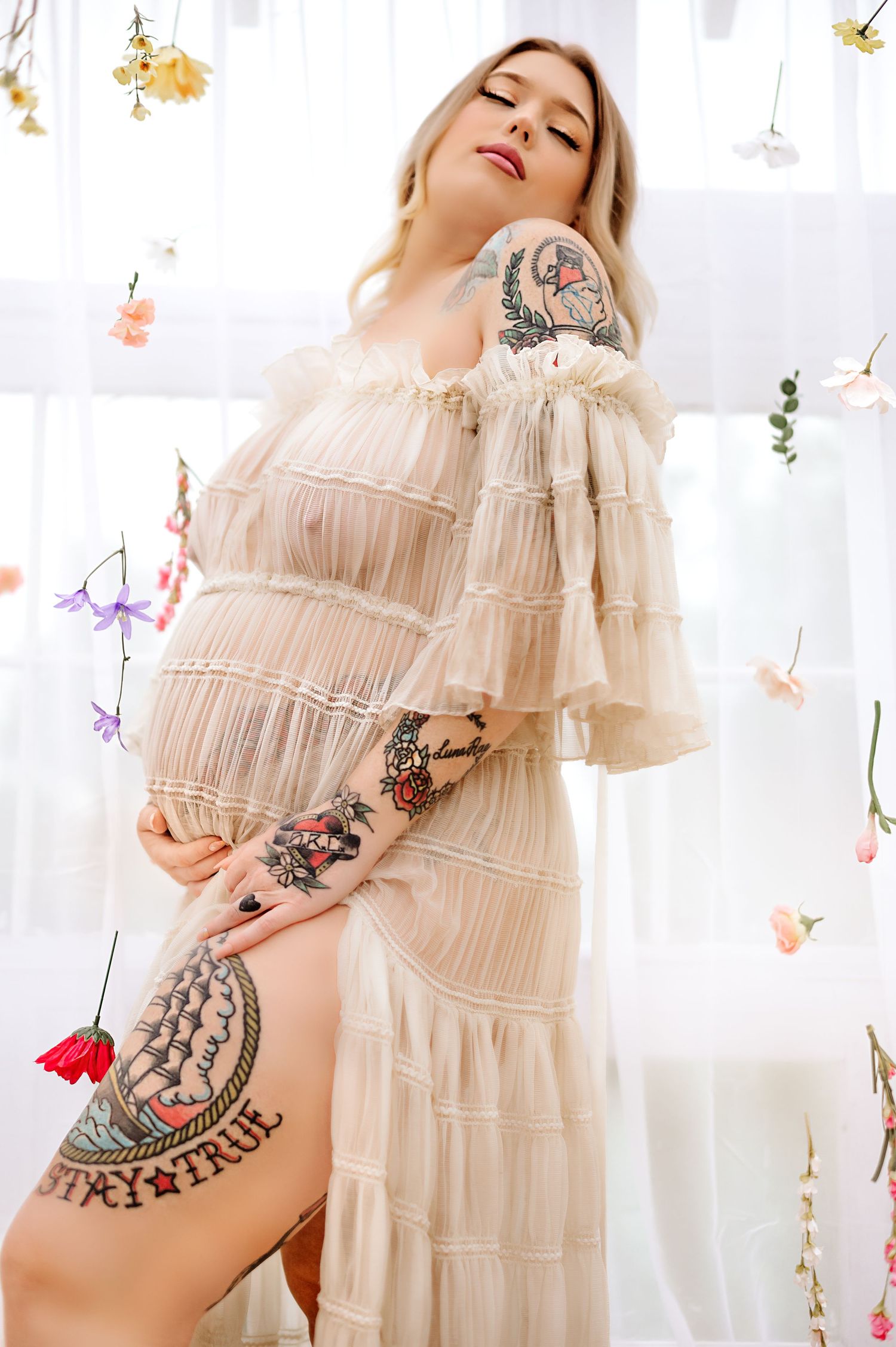 Ethereal portrait in flowing cream dress with visible tattoo art and floral decorations.