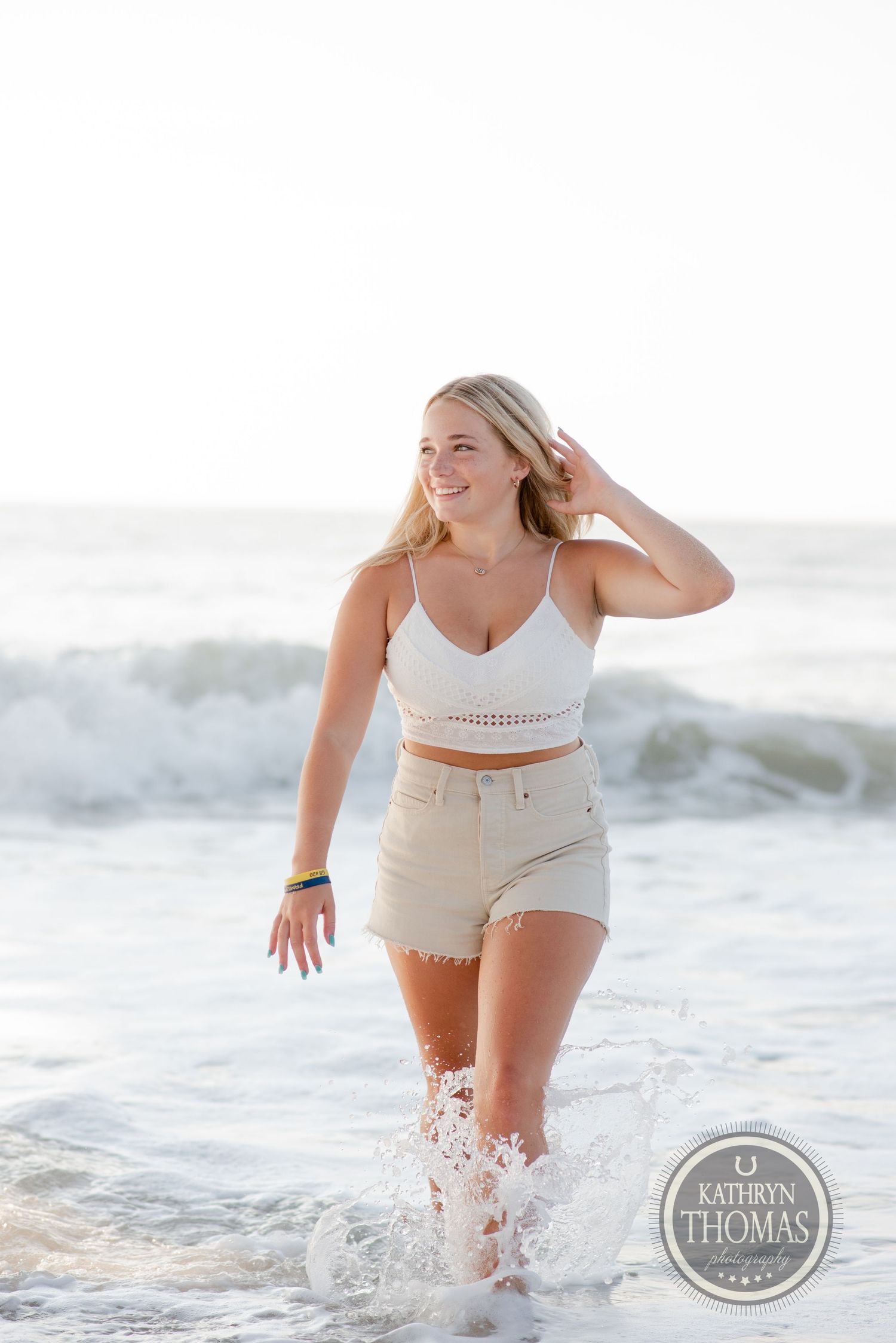 Someone splashing in ocean waves wearing white summer attire at the beach.