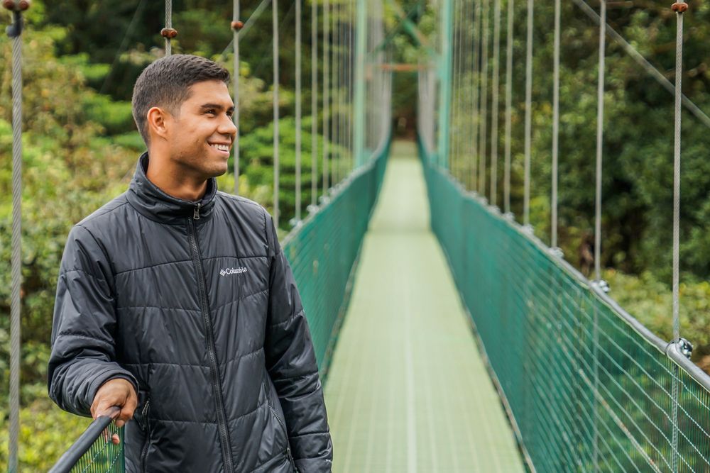 Tourist enjoying view from green suspended bridge in rainforest setting.