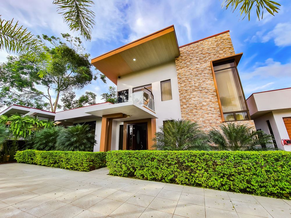 A modern luxury villa with stone accents and tropical landscaping under blue skies.