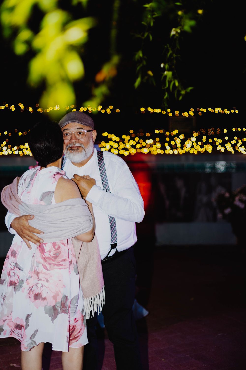 A couple shares an intimate dance moment under string lights at an outdoor reception.