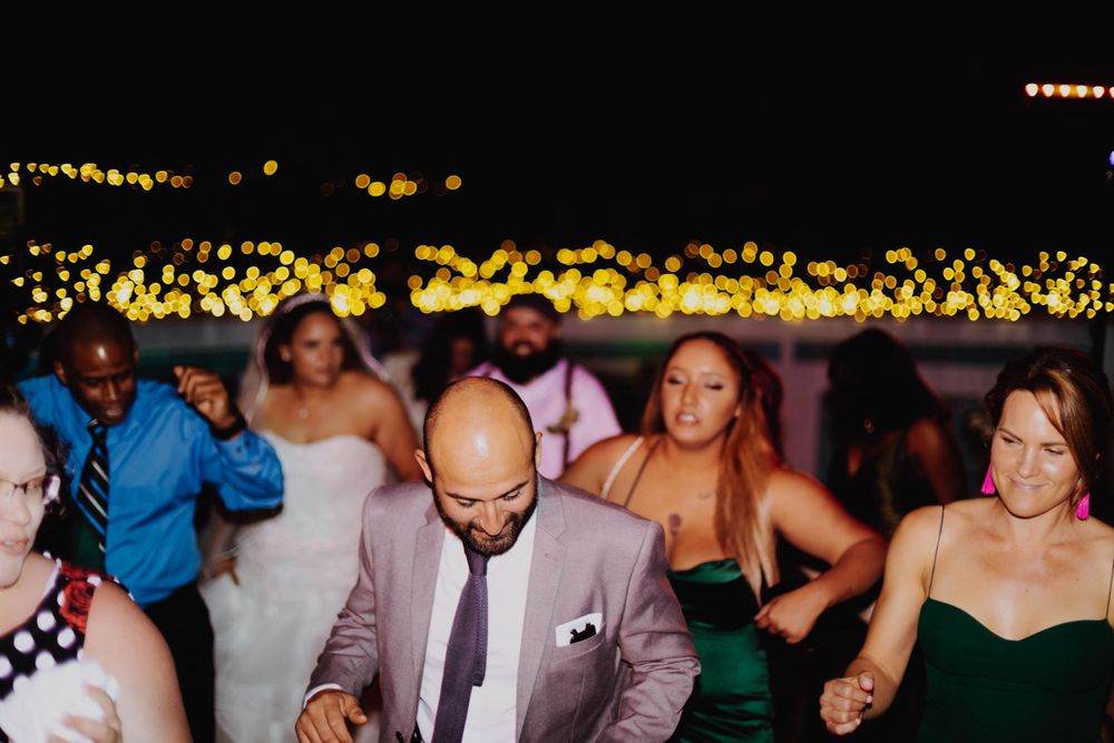 Wedding guests dancing and celebrating on the dance floor with string lights overhead.