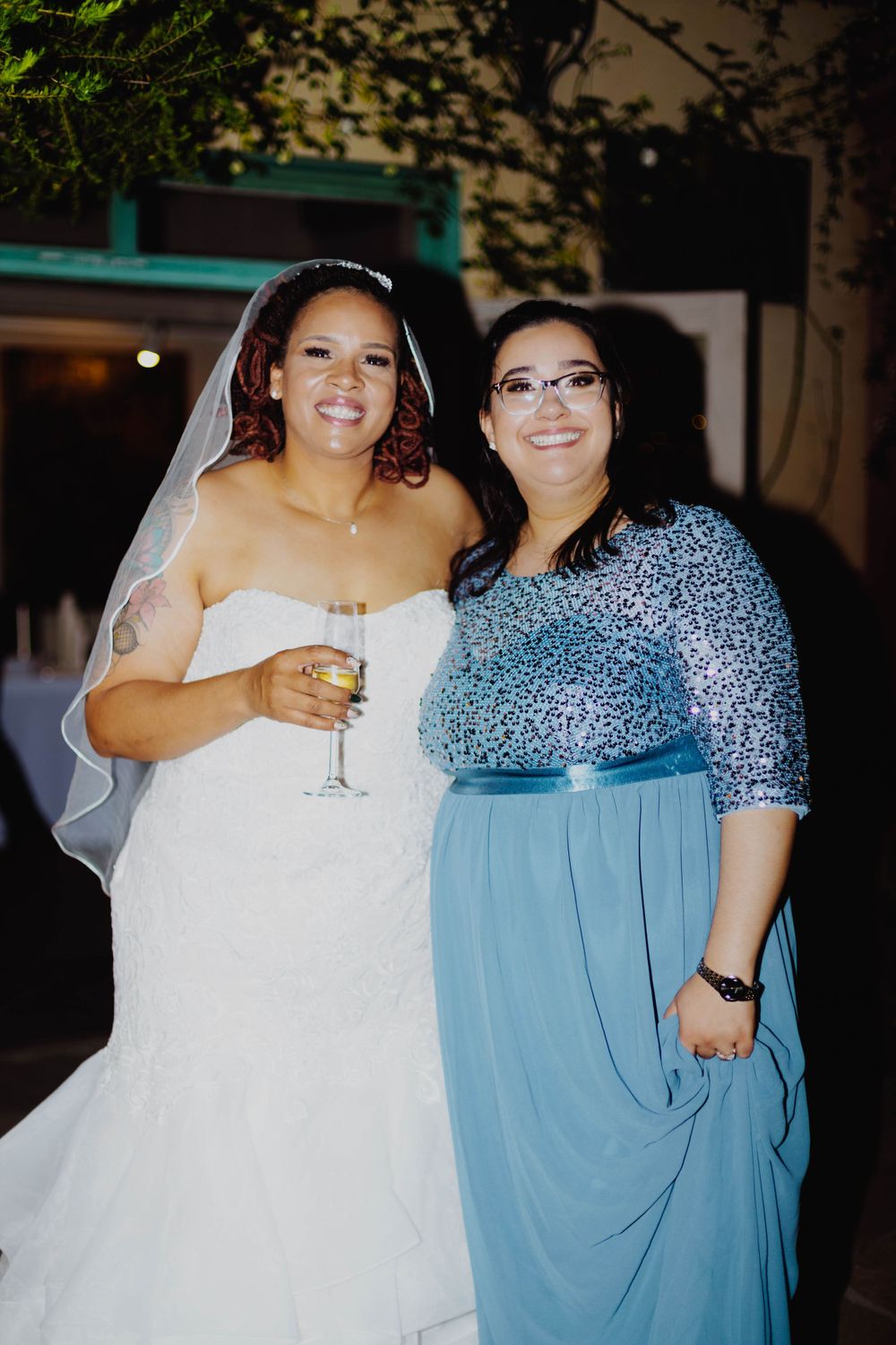 Two wedding guests posing together at an evening celebration with outdoor lighting.