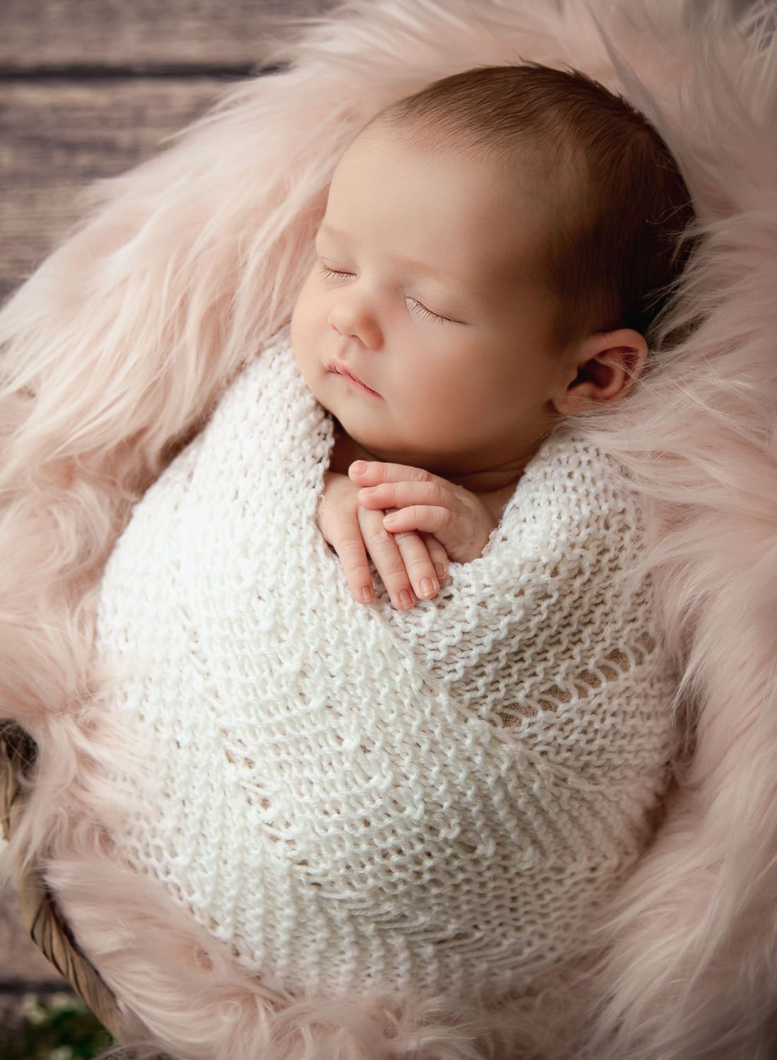 Posed newborn photoshoot with soft colours and fabrics and baby safely swaddled in a basket in Dubai