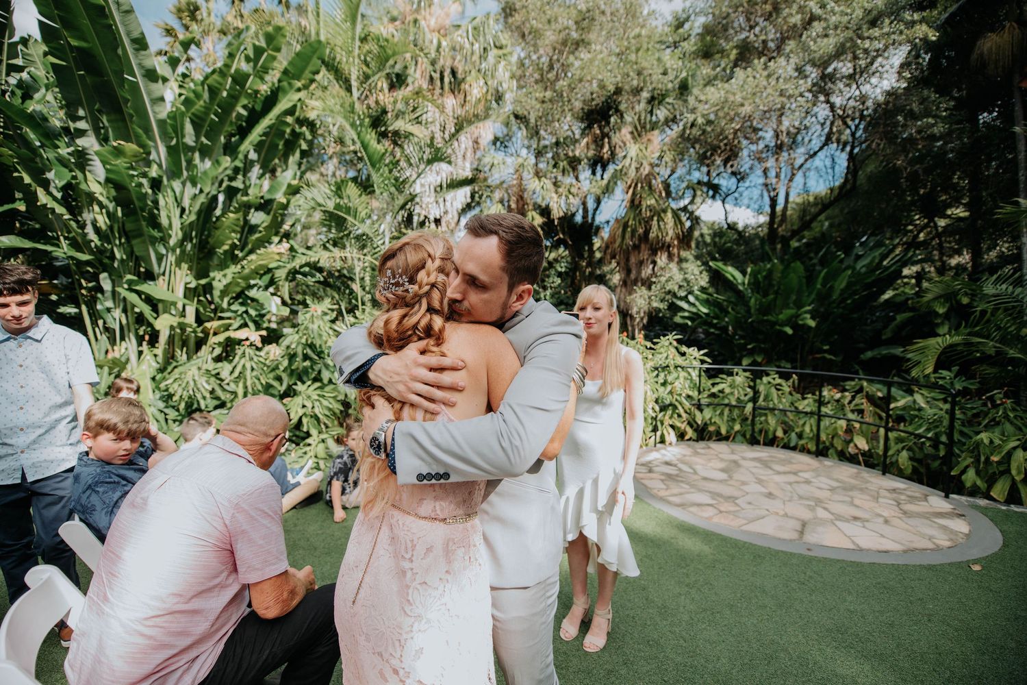 Romantic wedding moment captured in a lush garden setting with tropical foliage and a manicured lawn.