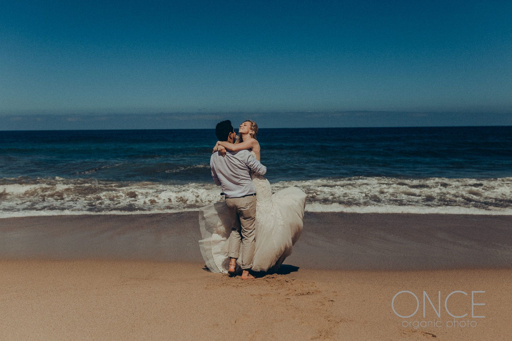 A romantic beach moment captured against the backdrop of crashing waves and blue ocean.