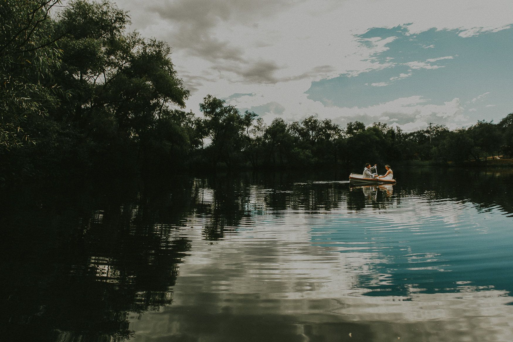 Serene lake view with boat silhouette against cloudy sky and tree reflections.