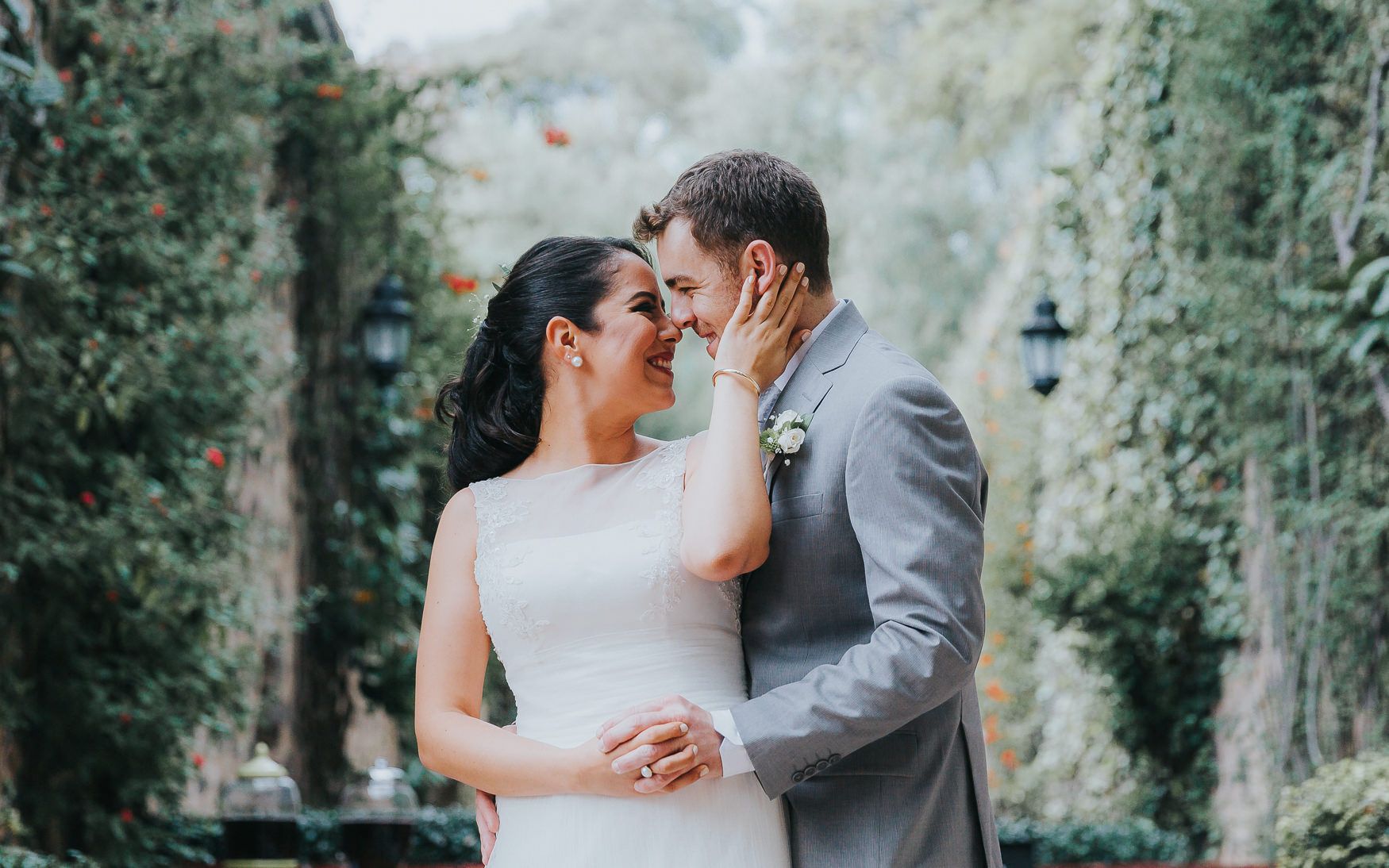 A couple shares an intimate moment in a garden path lined with greenery.