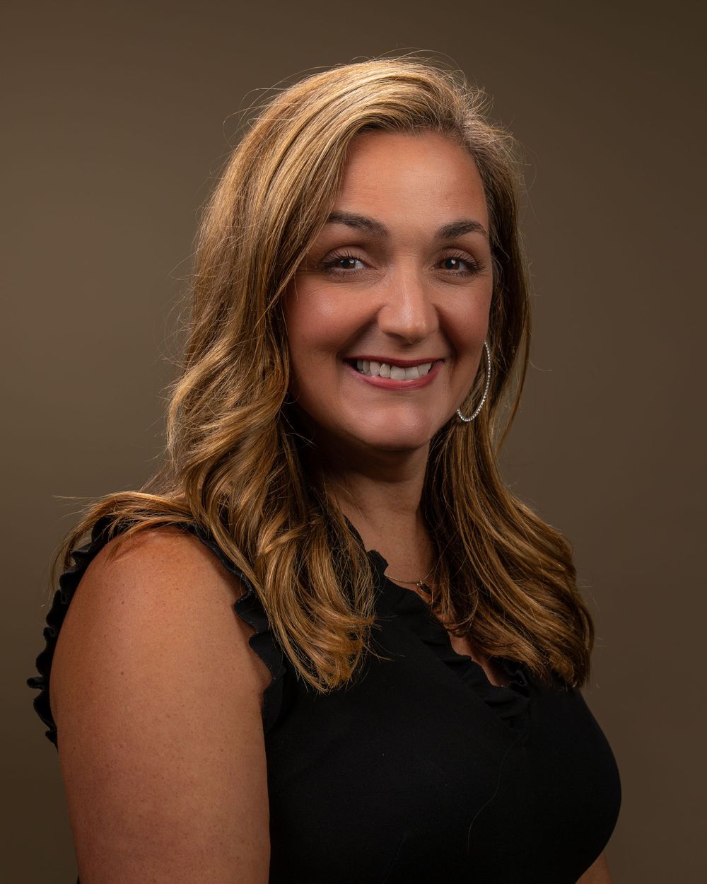 Professional studio portrait of person in black sleeveless top with styled wavy hair.