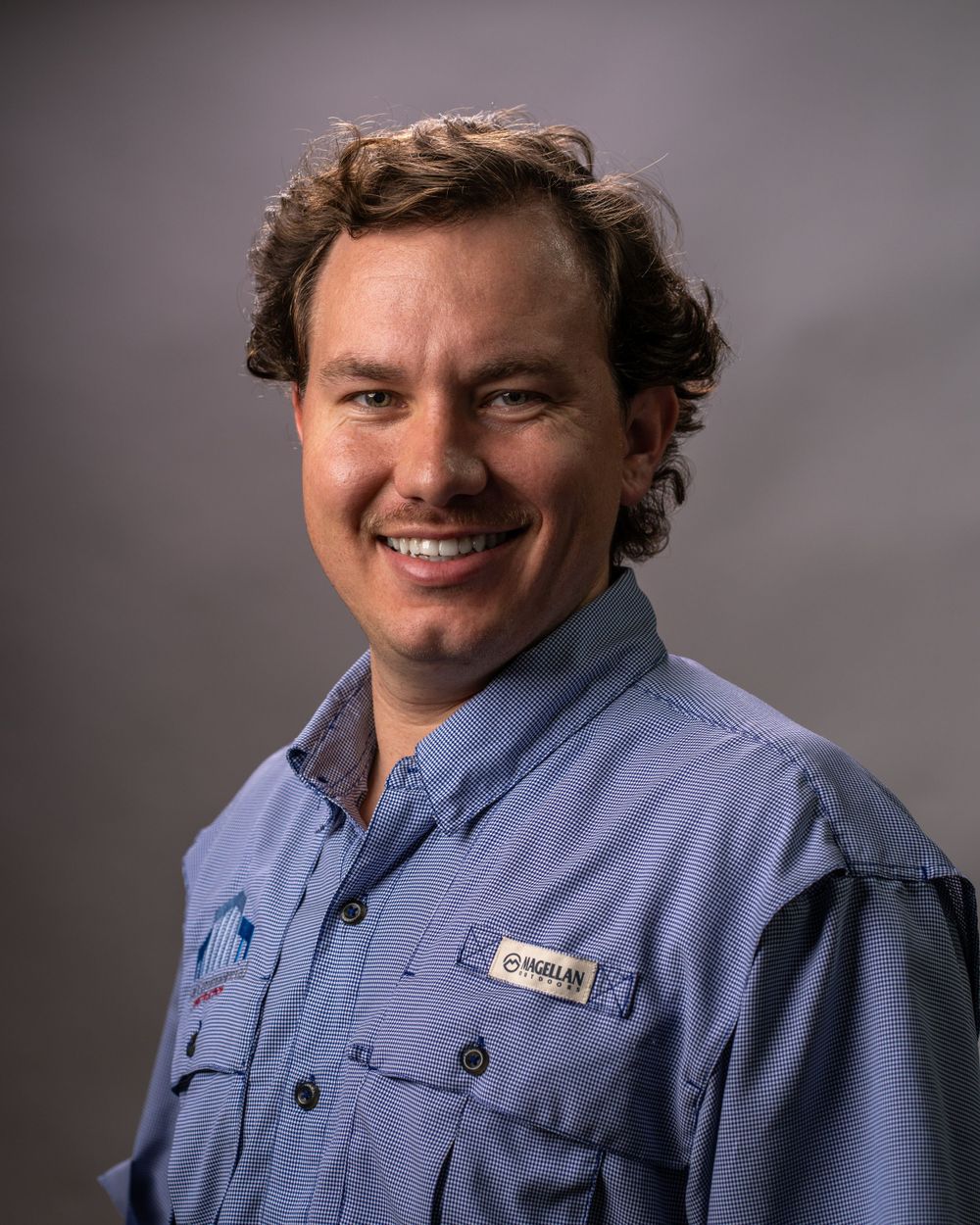Professional headshot of person in blue button-down shirt smiling at camera.