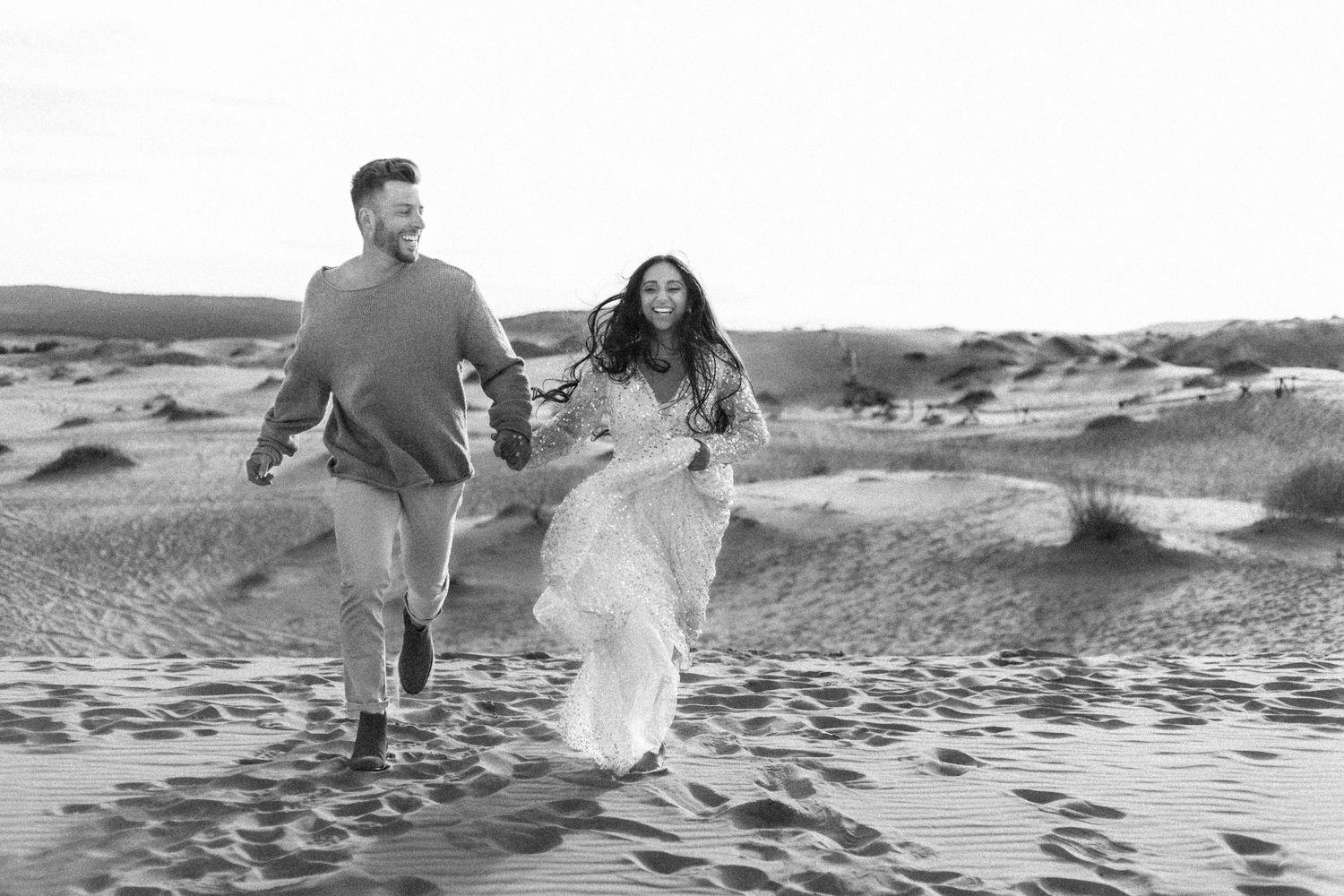 Couple running joyfully across sand dunes in black and white photography Coral Pink Sand Dunes, UT.