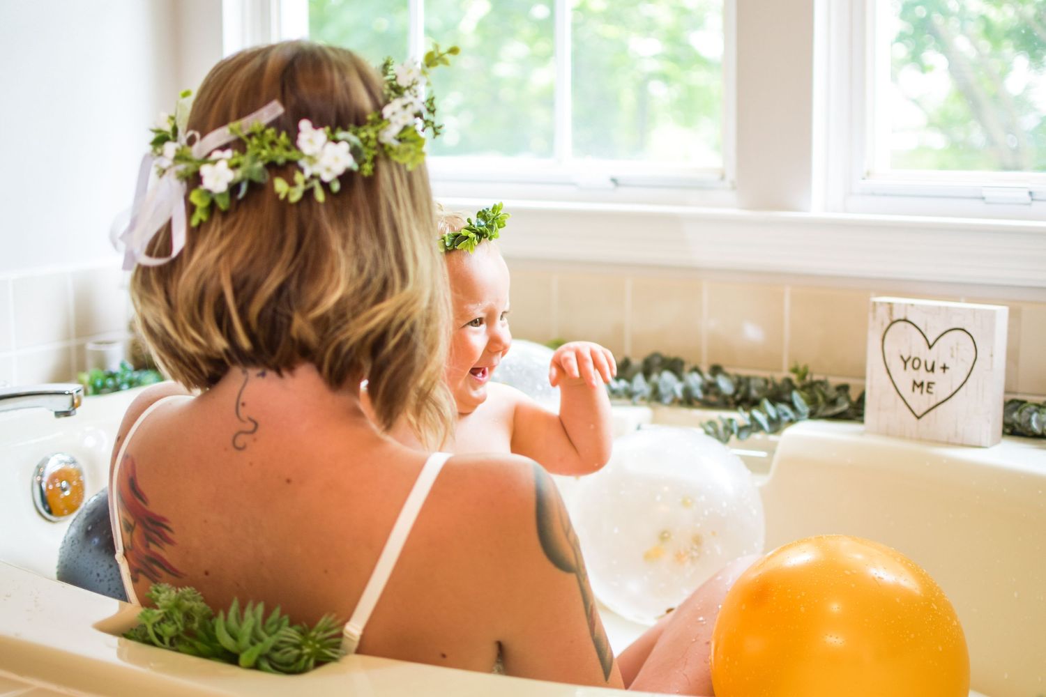 Person relaxing in floral bath with flowers and orange balloons.