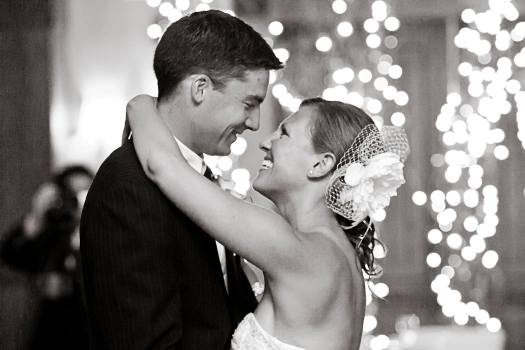 Wedding couple shares romantic kiss under twinkling lights at reception venue.