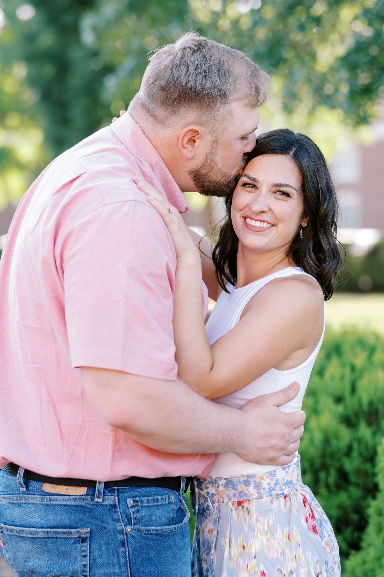 Couple sharing intimate moments in a sunny garden setting wearing pink and floral outfits.