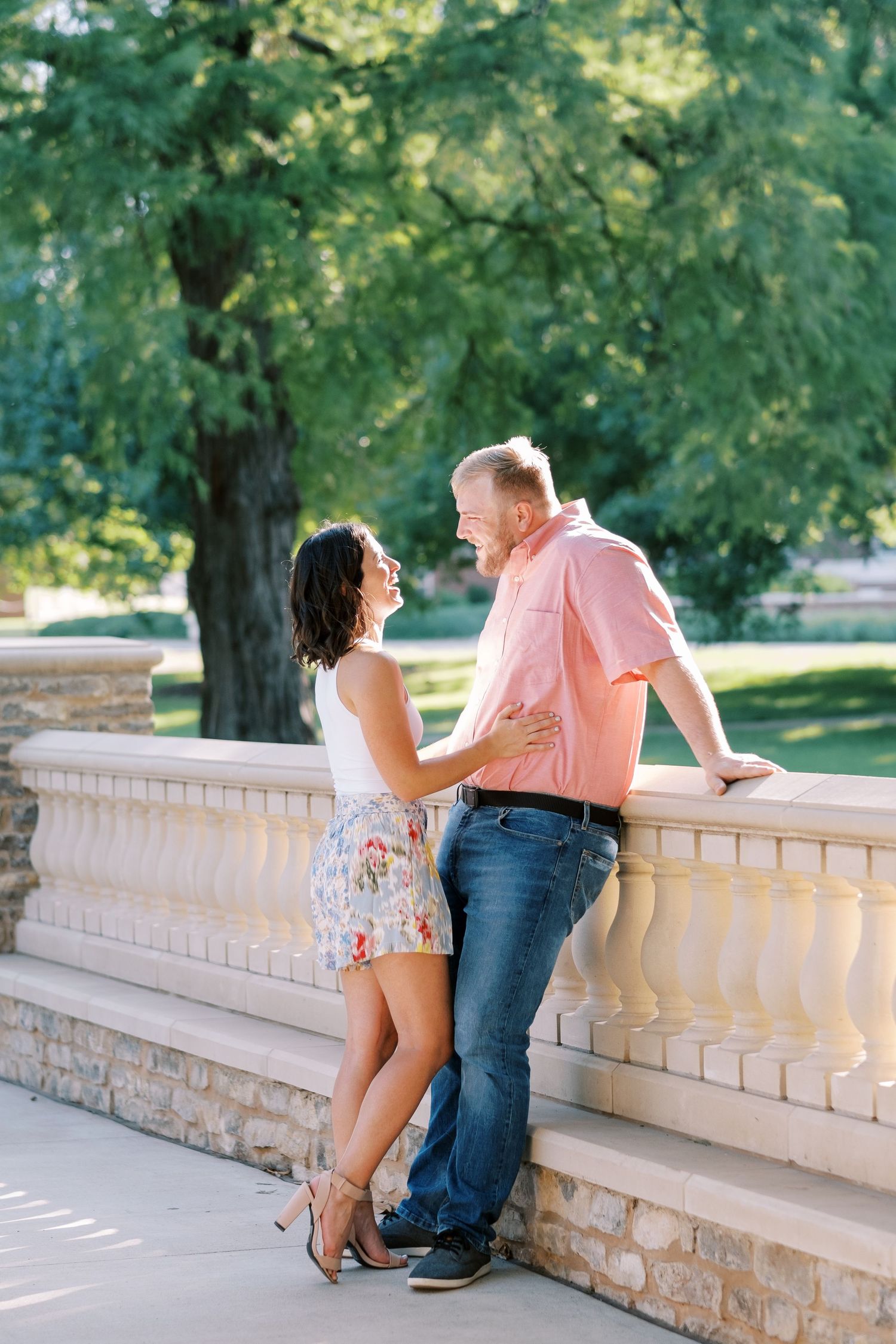 Couple sharing playful moments along a stone wall in a park setting.