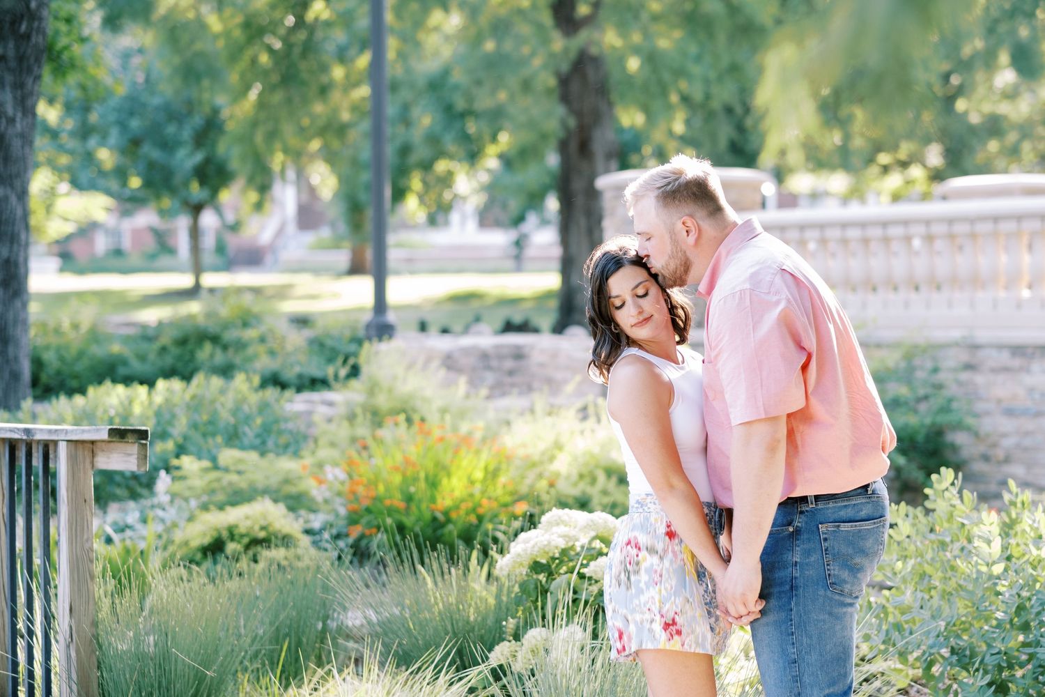 Candid engagement photos captured in a lush garden setting with natural sunlight.