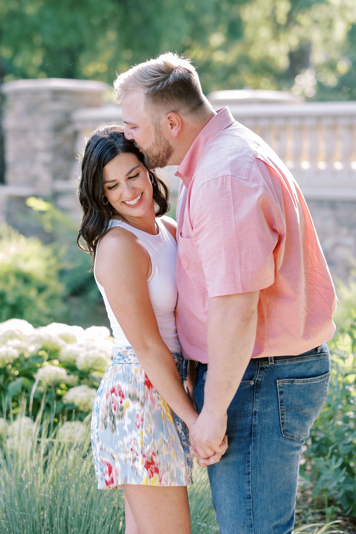 A romantic couple shares an intimate moment outdoors in summer attire against a garden backdrop.