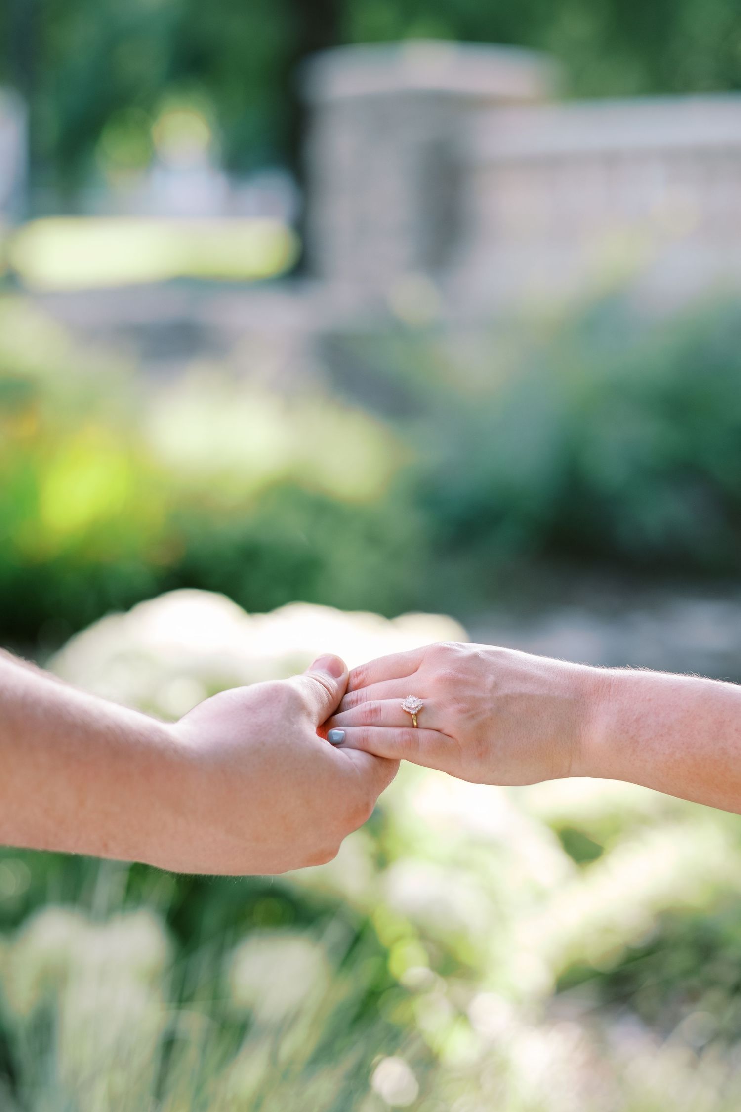 Close-up of hands with engagement ring in soft focus against blurred garden background.
