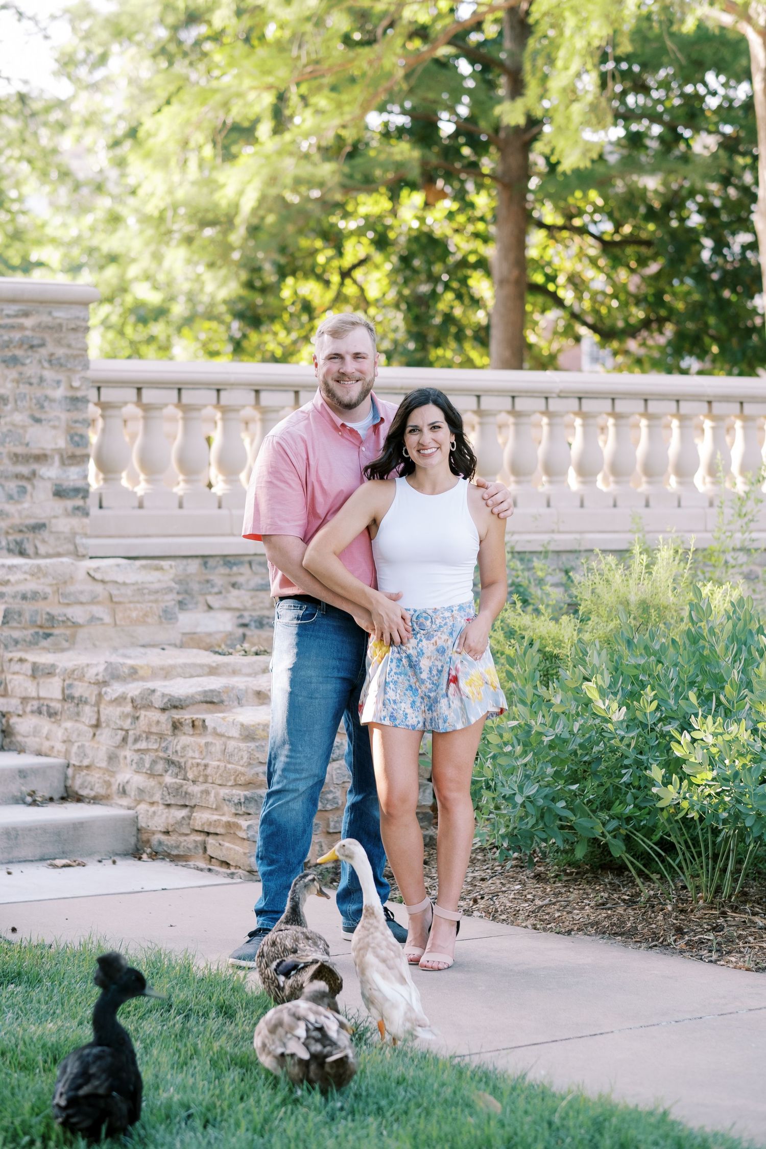 A couple poses on stone steps with their dogs in a garden setting.