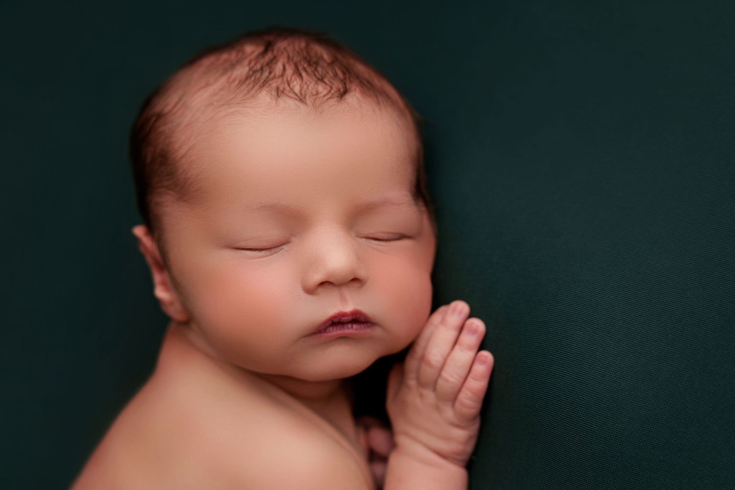 Peaceful sleeping newborn baby with closed eyes on dark green background.