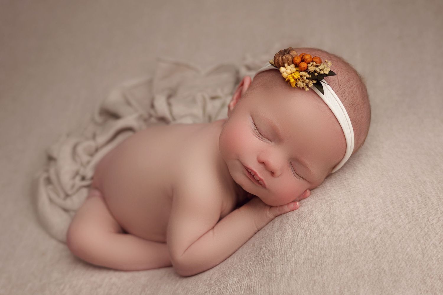 Sleeping newborn photographed in natural light on beige blanket wearing delicate floral headband.