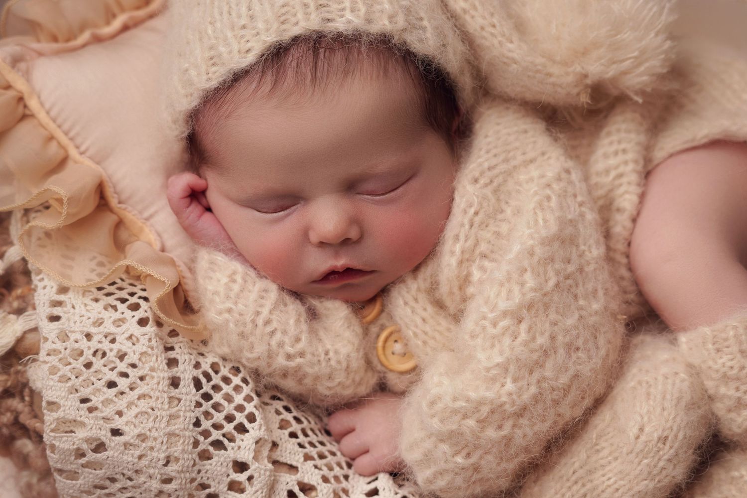 A peaceful sleeping newborn swaddled in soft cream-colored knit blankets and delicate lace.