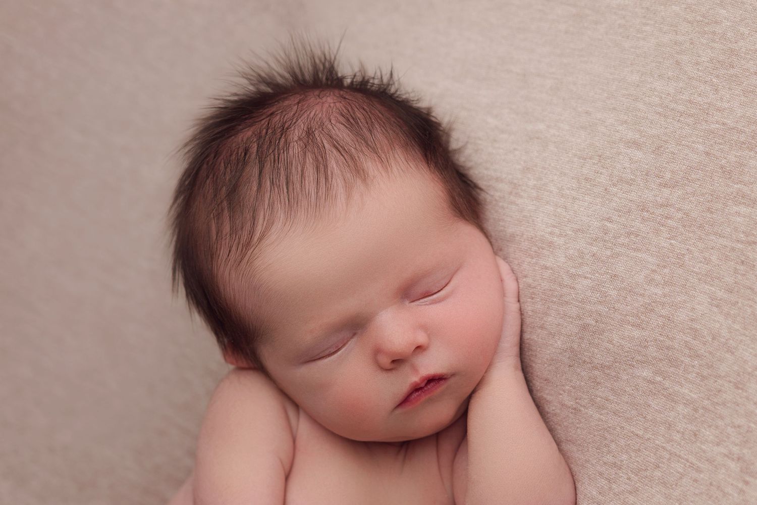 Sleeping newborn baby rests peacefully on soft beige blanket during professional portrait session.