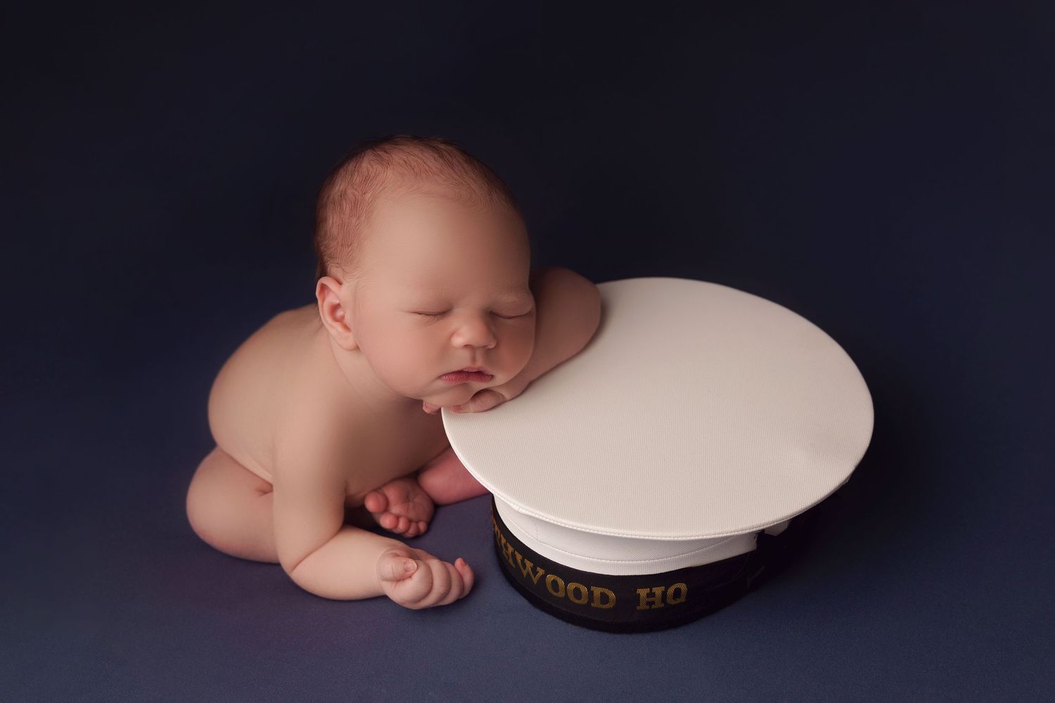 Newborn baby peacefully sleeping on a white sailor's cap against dark background in professional studio setting.