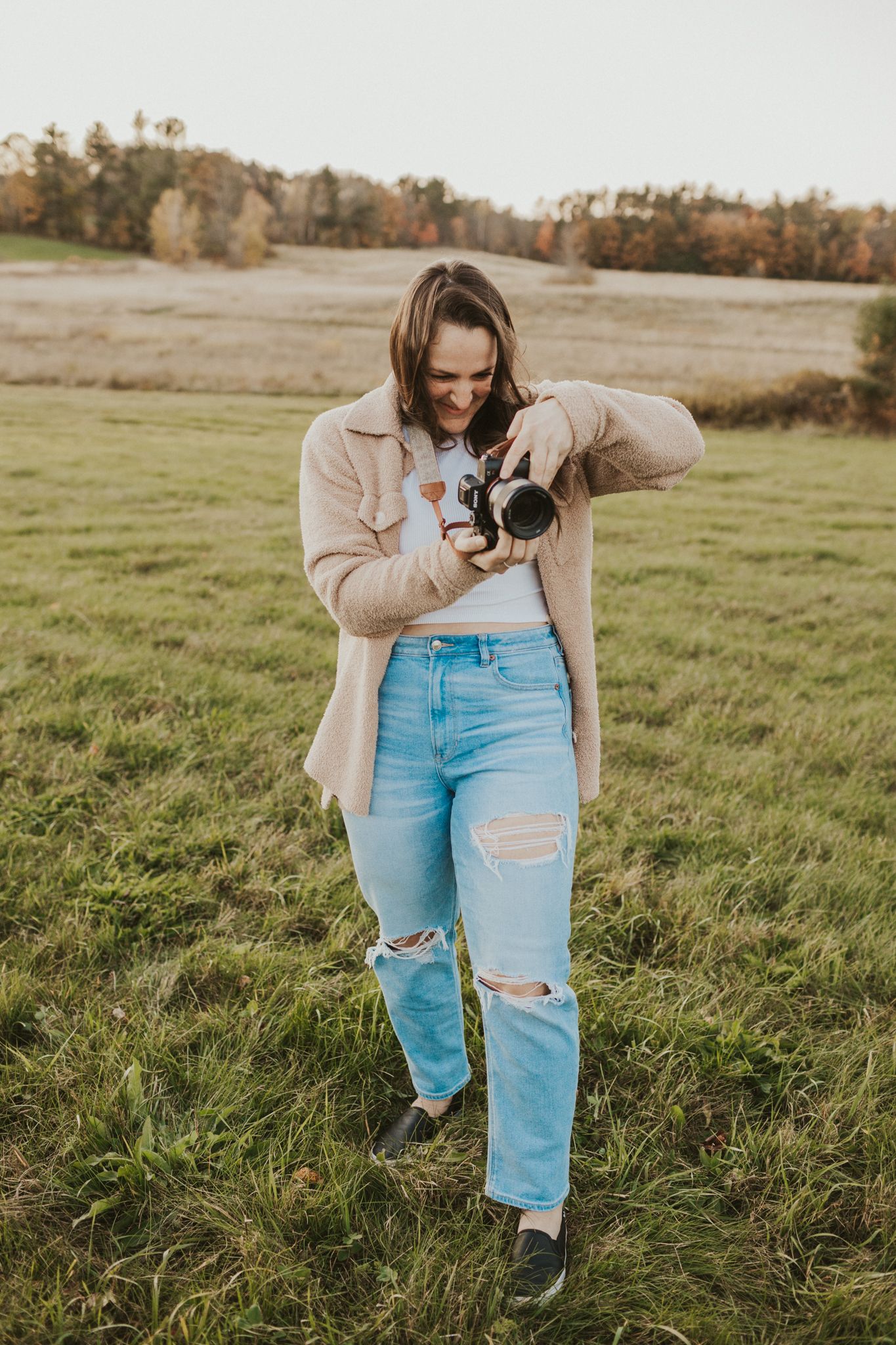 Person in beige sweater taking photos in autumn field.