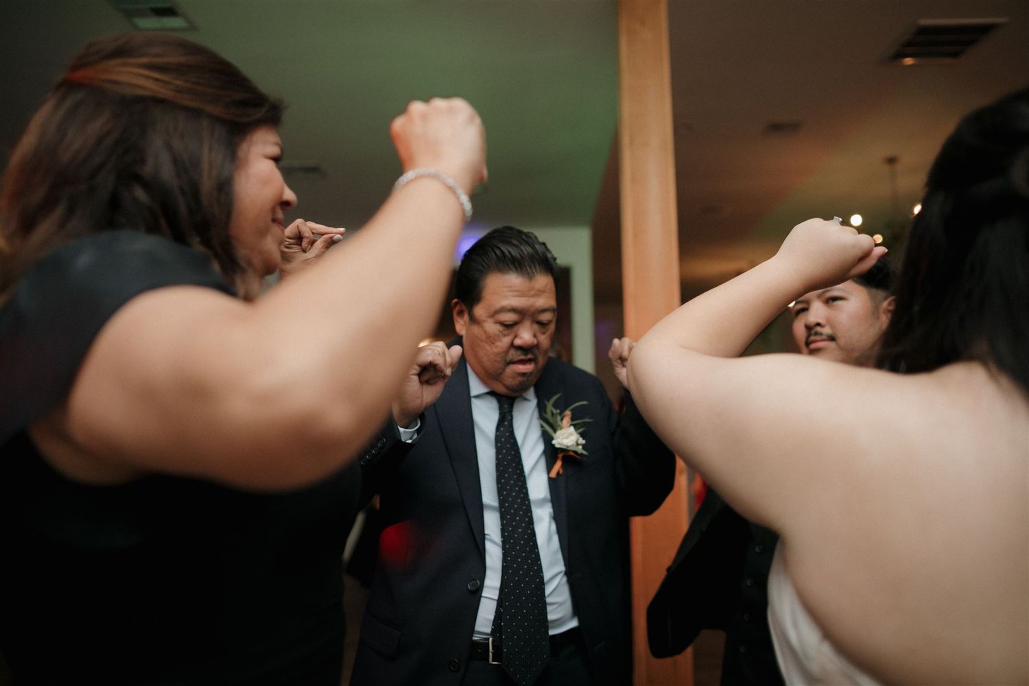 Wedding guests dancing energetically with arms raised in celebration at an indoor reception.