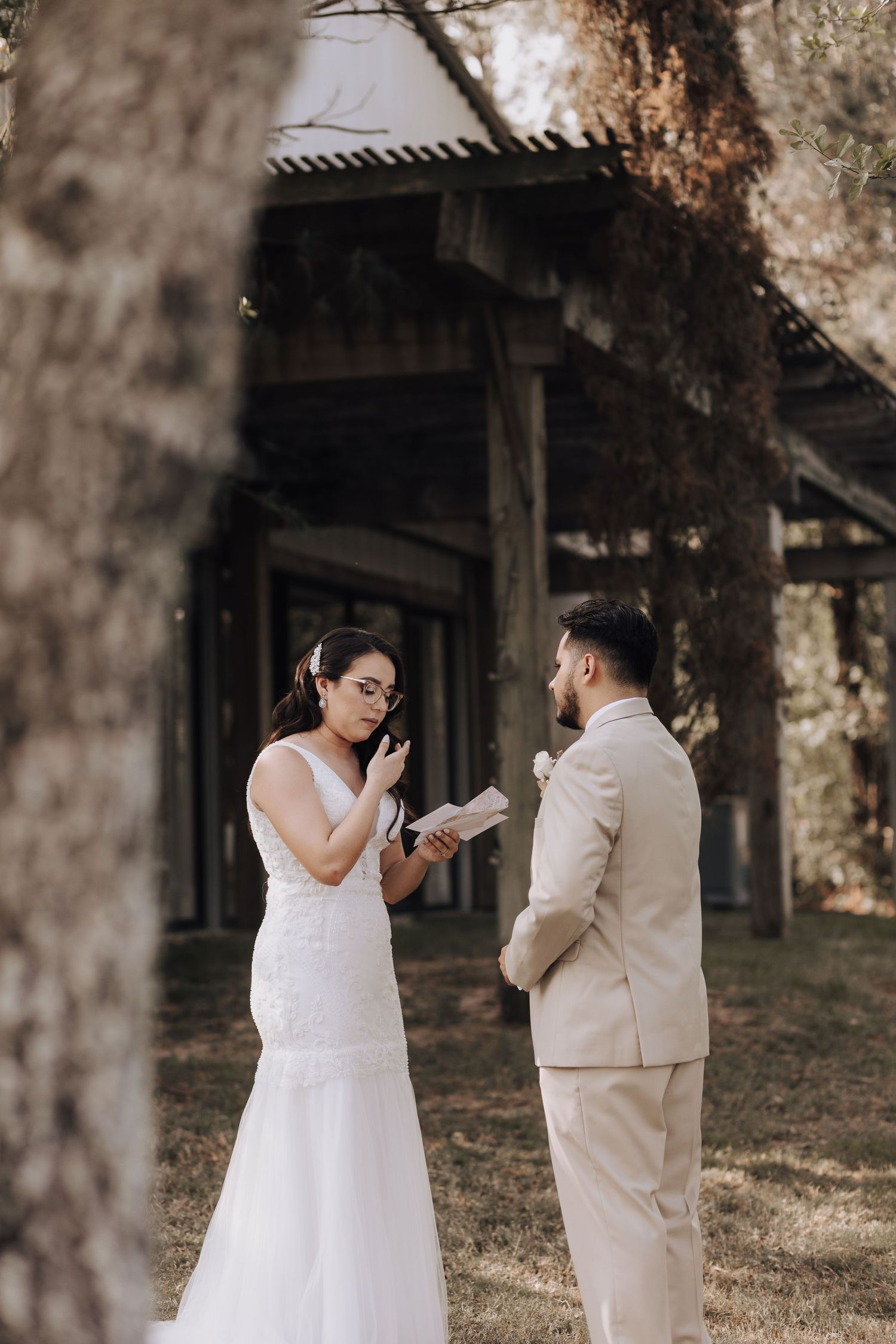 Private vow exchange between couple in front of rustic wooden building during wedding ceremony.