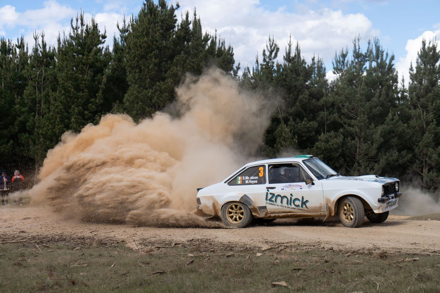 White rally car kicking up dust while drifting through a dirt course.