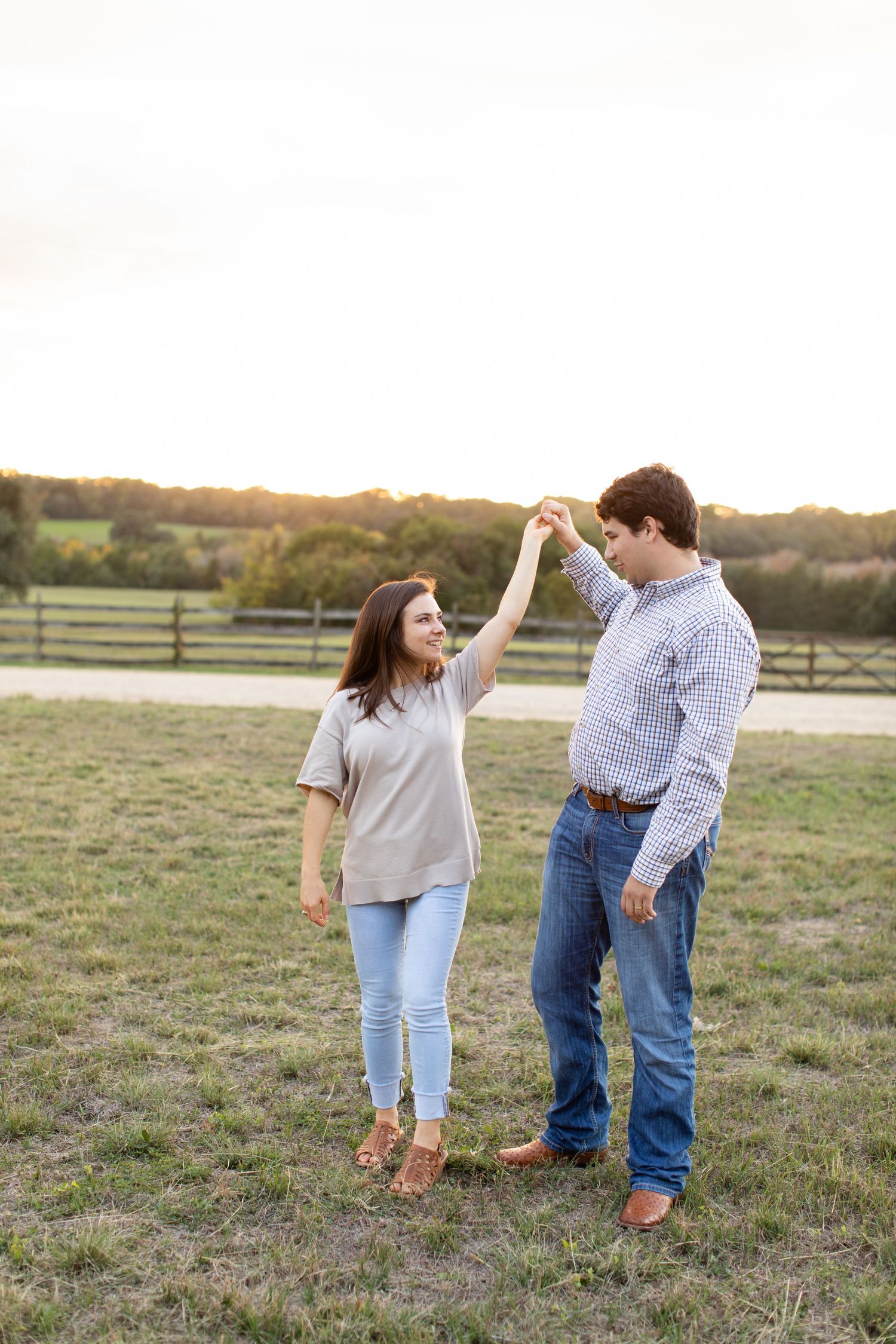 Couple dancing and twirling in a countryside field during golden hour.