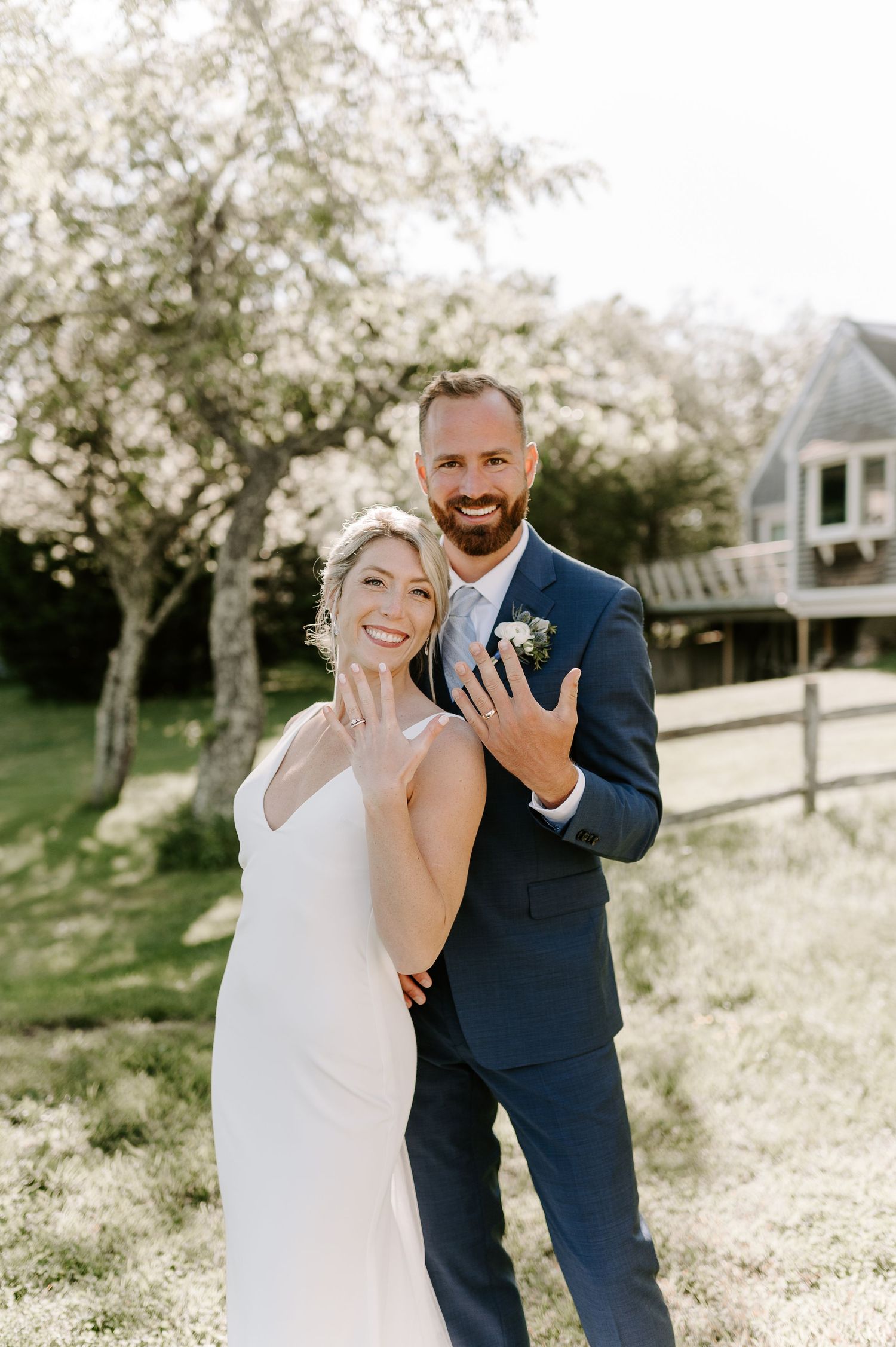 Joyful wedding couple showing off their rings in a sun-drenched outdoor setting.