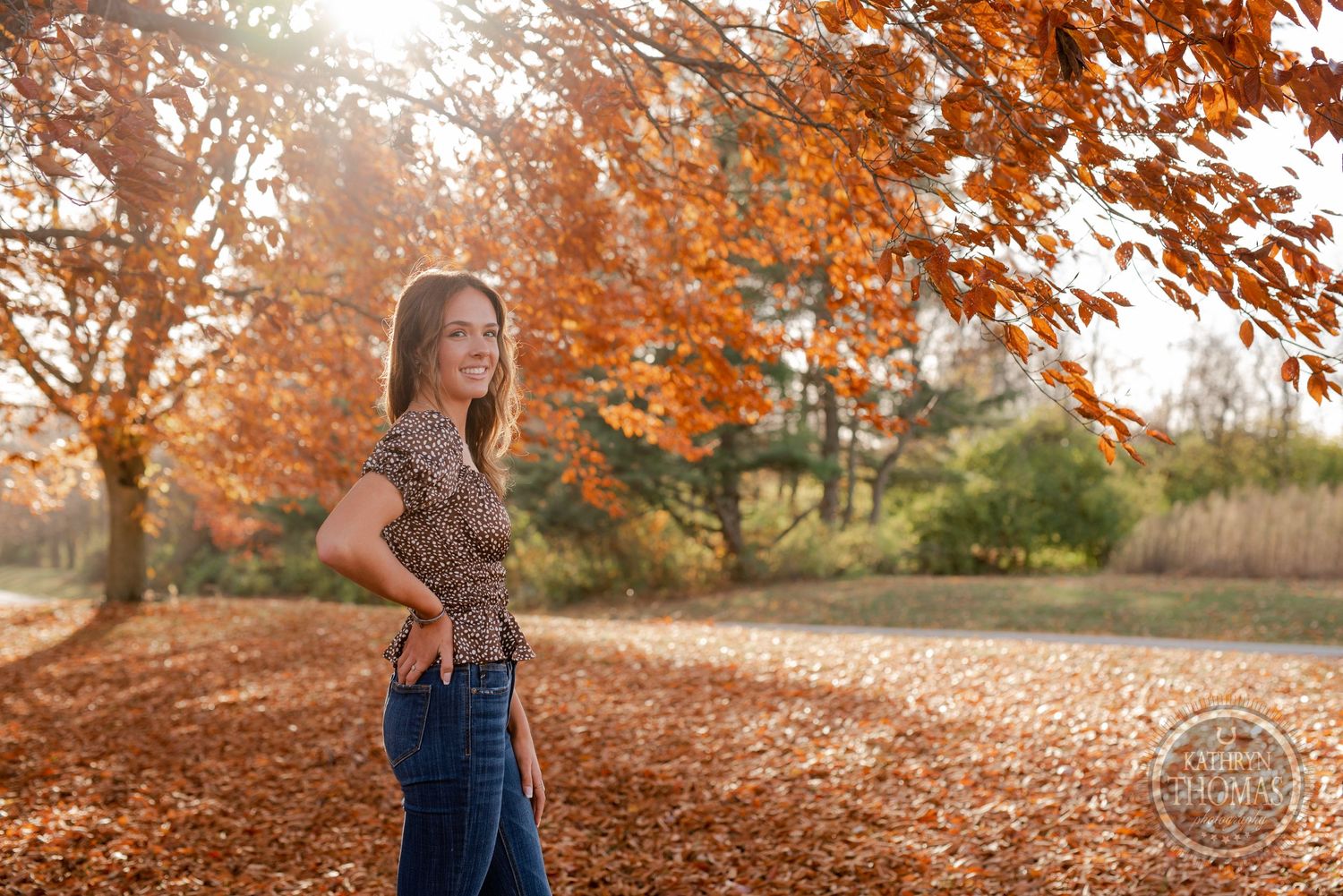 A casual outdoor portrait with vibrant autumn foliage and golden sunlight.