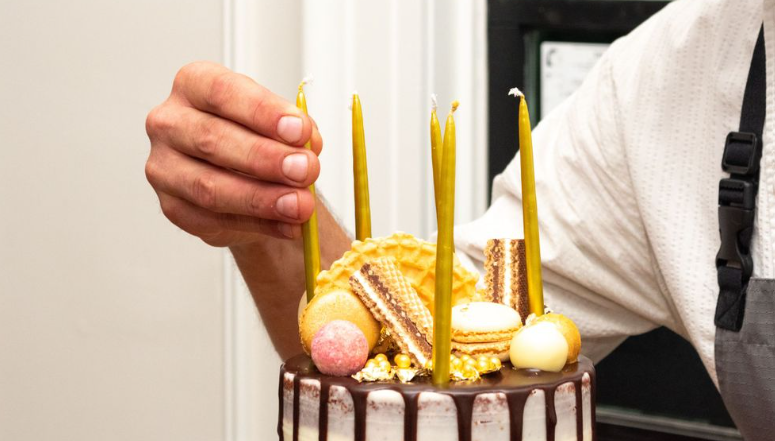 Hands placing golden candles on a chocolate birthday cake.