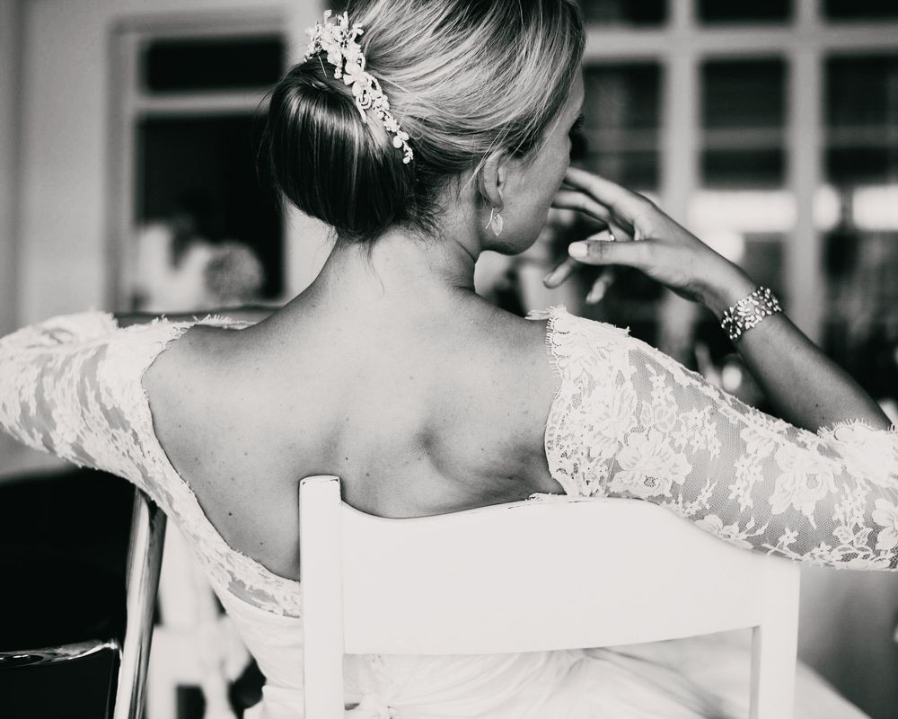 Close up black and white photo showing delicate lace details of a wedding dress and bridal hairstyle from behind.