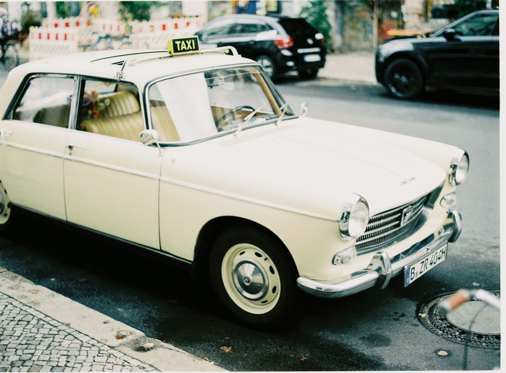Vintage white Peugeot taxi parked on a cobblestone street in a European city setting.