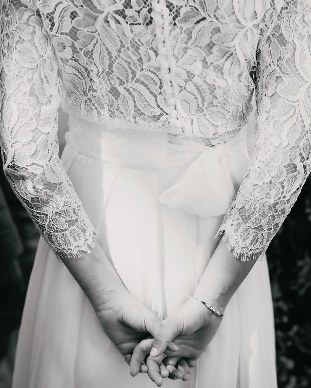 Detail shot of white lace sleeves and clasped hands on a wedding dress.