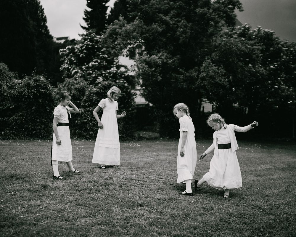 Vintage black and white photo of people in long white dresses dancing or playing in a garden.