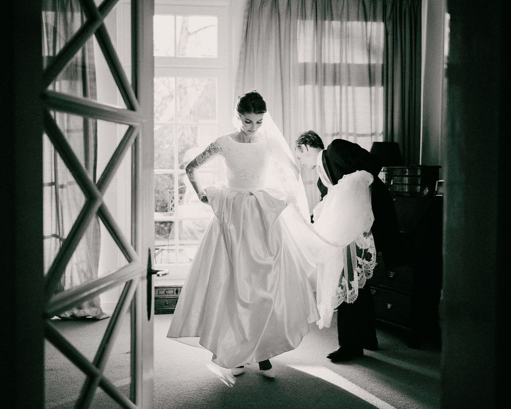 Black and white photo showing the preparation of a wedding dress in a sunlit room.