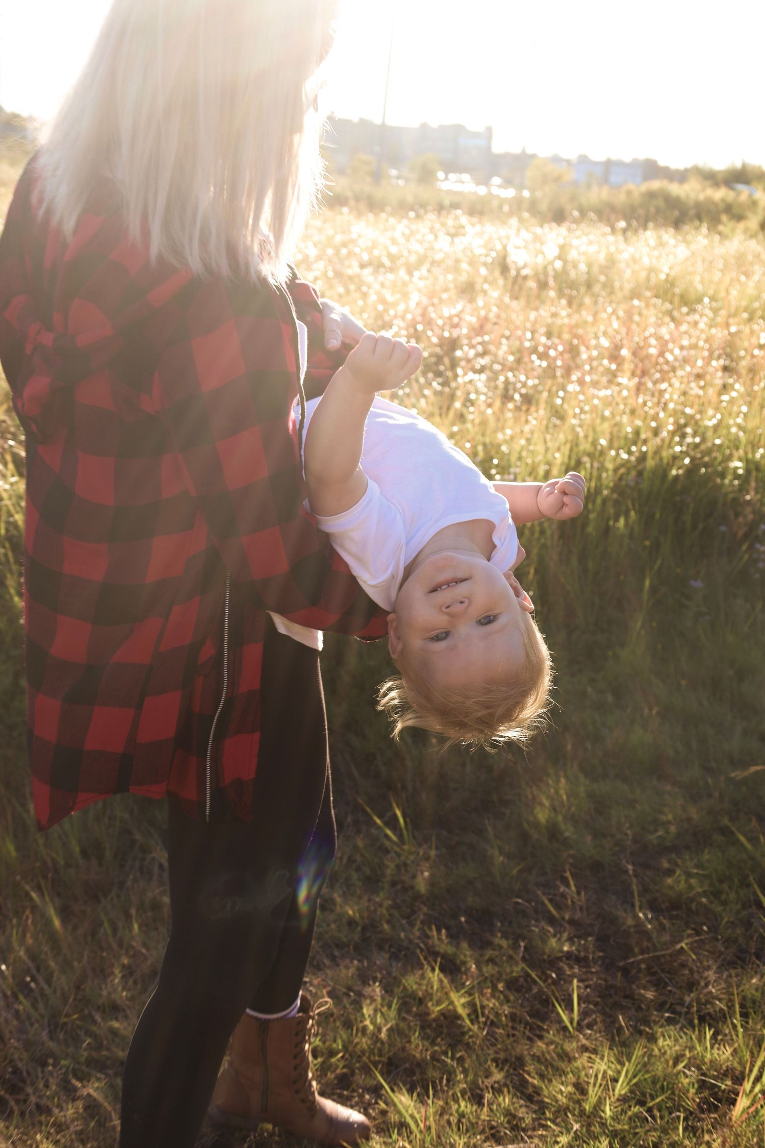 A couple embraces in a golden field at sunset wearing red plaid and white.