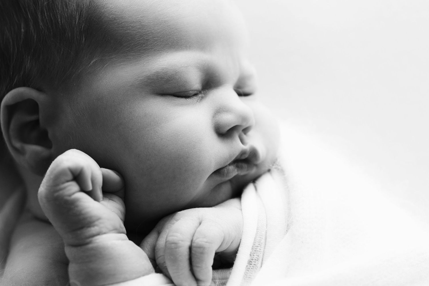 Close-up black and white portrait of a peaceful sleeping newborn baby with tiny hands.