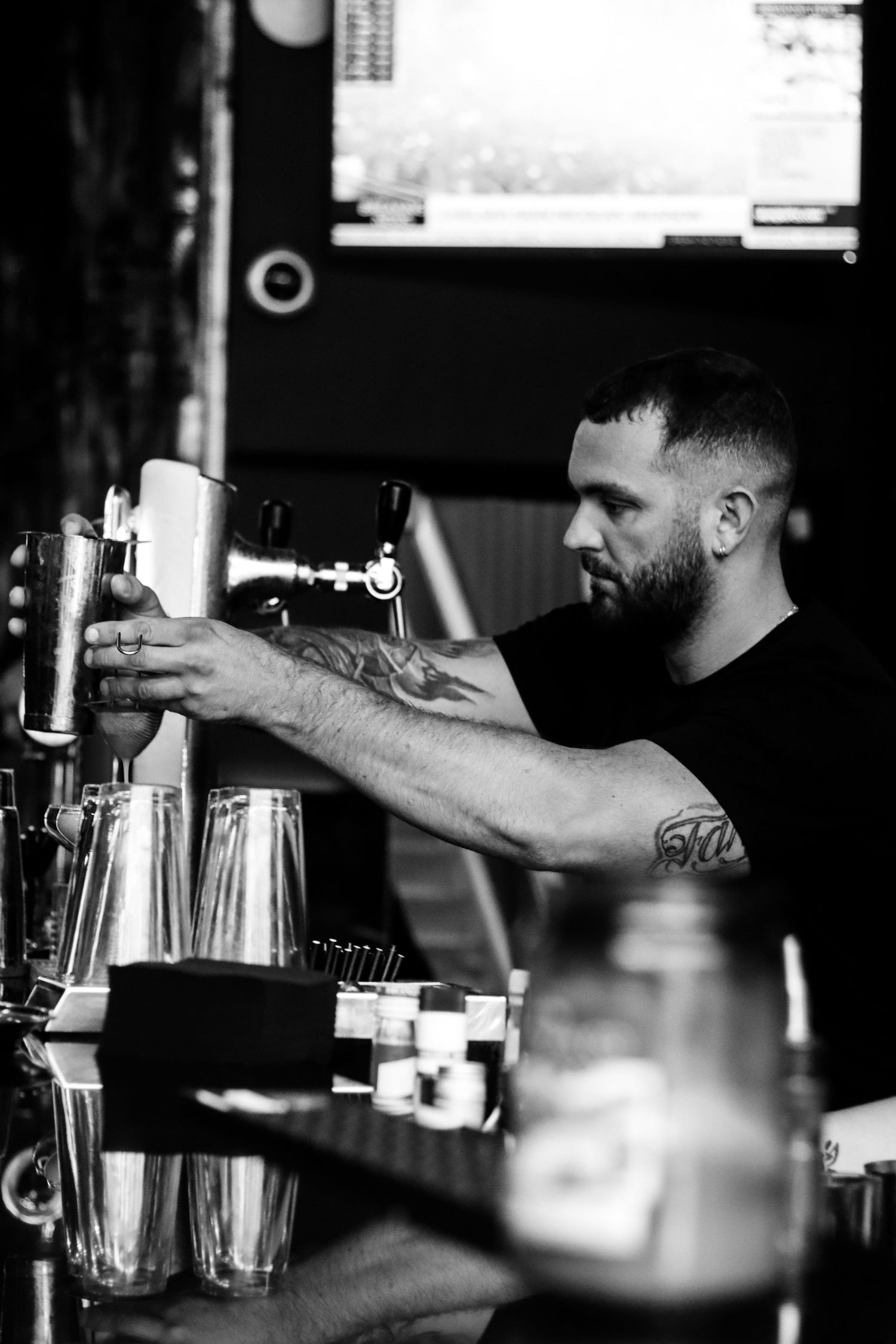 Bartender operating beer tap at bar counter in black and white photography.