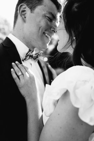 A tender black and white close-up moment between newlyweds showing rings and formal attire.