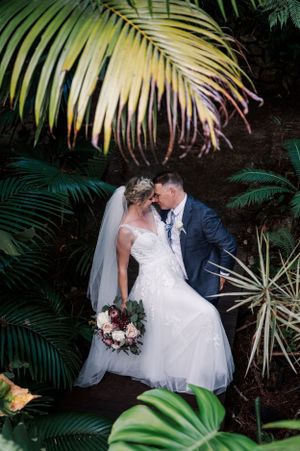 Tropical garden wedding scene with palm fronds framing the elegant couple.